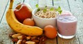 Picture of a banana, fruit smoothie, bowl of cereal, apple, satsumas and nuts