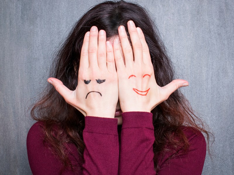 Girl with her hands over her face which have a happy and sad face drawn on them