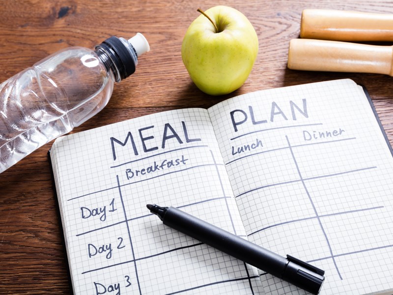 Meal plan journal with a pen along with an apple and a bottle of water