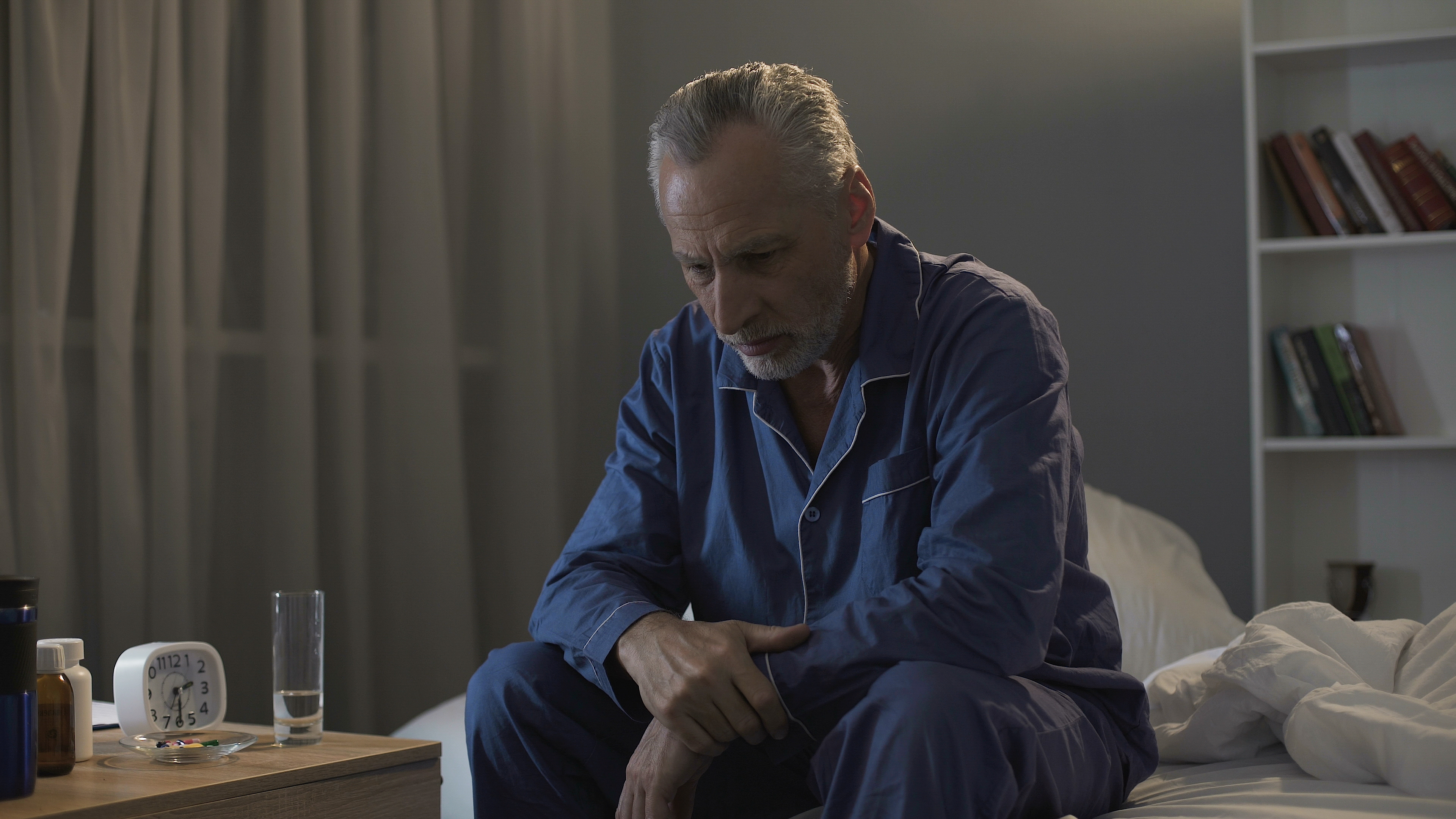 Man sitting on bed in pyjamas looking tired